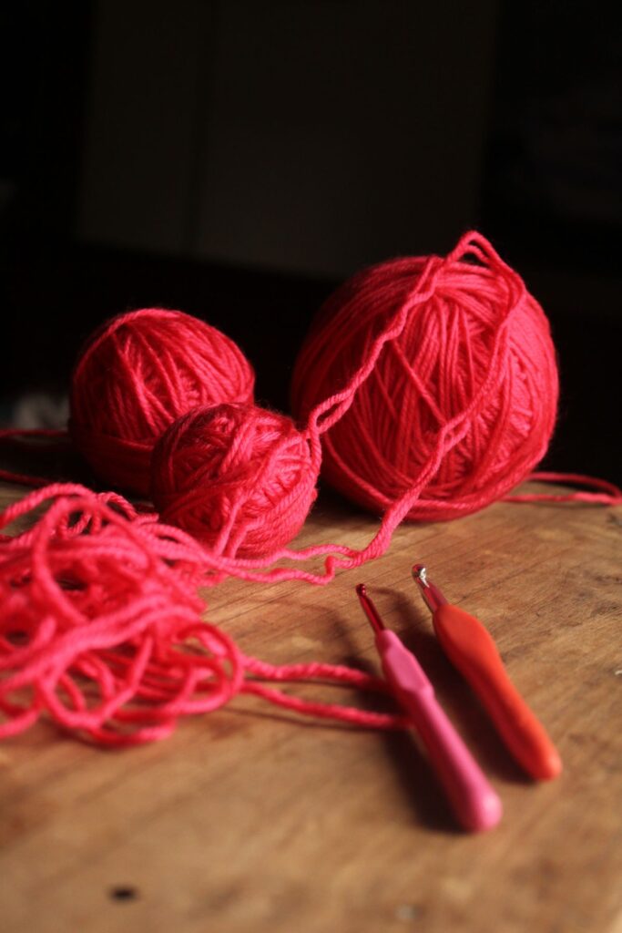 Vibrant red yarn and crocheting hooks on wooden table